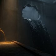 Enorme cisterna en penumbra: por una brecha en la pared sale un torrente oscuro y silencioso, mientras que de un pequeño tubo en el lado opuesto cae un hilo fino de líquido ámbar luminoso, minúsculo en comparación
